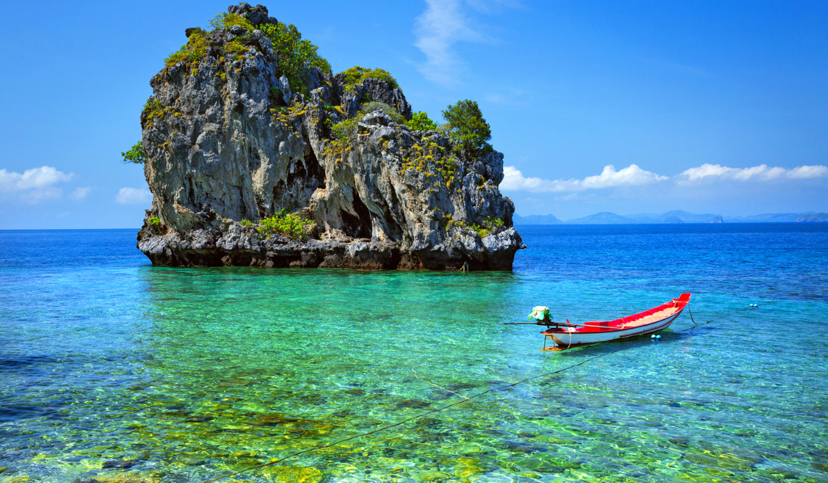 Phuket beach with turquoise water, palm trees, and tourists relaxing.